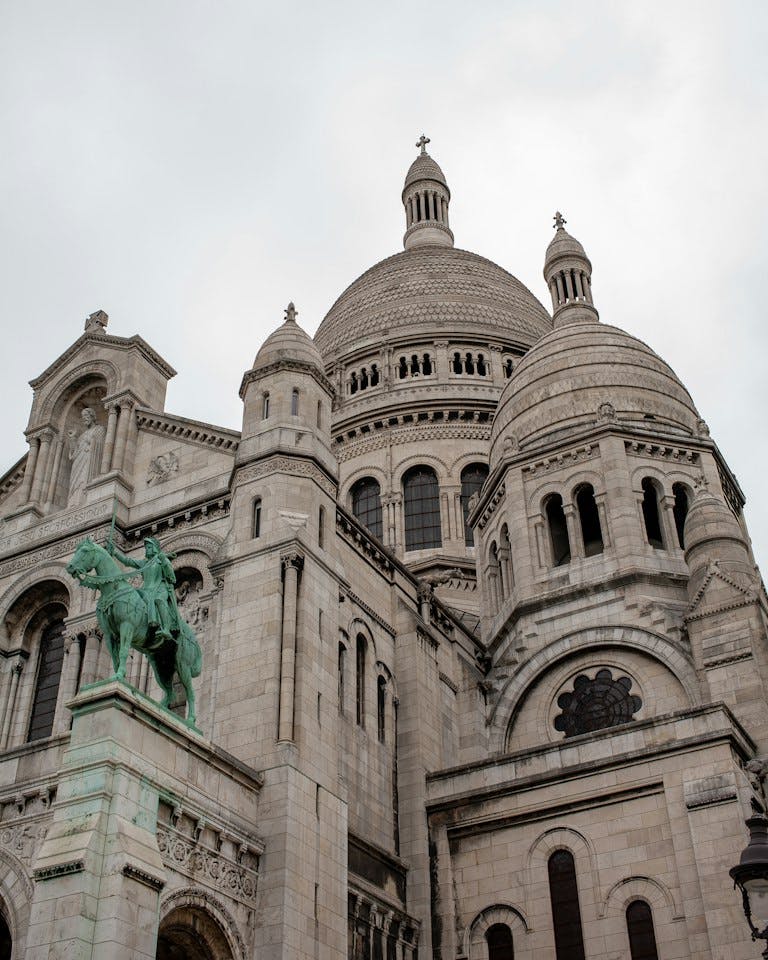a large stone building with a statue in front of it with Sacré-Cœur, Paris in the background